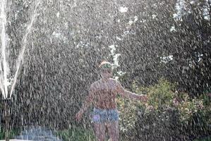 happy girl runs through a fountain in a green park in the sunshine photo