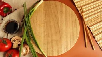 Round wooden board, sauce and various vegetables on the table, wooden stick on a brown background. Flat lay. Copy space in the center of the frame for your text or logo. Recipe and Cooking photo