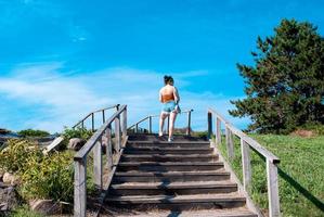 Rear view of a young woman in short shorts climbing stairs in a summer park on a sunny day photo