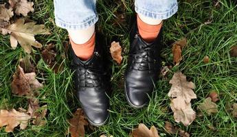 Female legs in black boots on green grass with yellow fallen autumn leaves in the park. Autumn concept. Womens shoes in autumn foliage photo