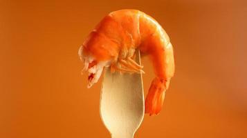 One large king cooked shrimp in the sink on a wooden fork on a brown background. Infrastructure of crustaceans of the decapod, eating carrion. Sea delicacy. Shrimp is used in cooking. Beer snack photo