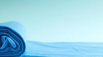 One roll of plastic trash bags in blue on a blue background. Bags that are designed to accommodate garbage in them and used at home and placed in various garbage containers. Copy space photo