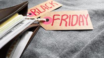 Brown wallet with money, dollars on a blue background, jeans texture, cardboard tag with red text Black Friday. Black Friday - International day of purchases, promotions, discounts, sales. photo