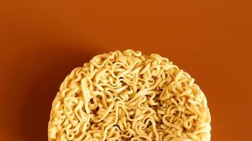 Korean instant noodles in the shape of a circle on a brown background. A yellowish-white dried raw vermicelli with long round lines and twisted in different directions into a briquette. photo