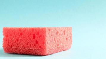 One red sponge on a blue background is used to wash and erase the dirt used by housewives in everyday life. They are made of porous material. Saving detergent, which allows you to use it sparingly photo