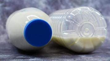 A half-empty and full plastic bottle of fresh regular milk lies on a dark gray marble or concrete backdrop. Close-up front view. World milk day concept. Nutrient fluid. photo