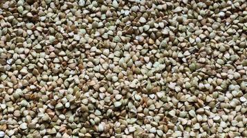 Background from raw organic green buckwheat porridge, vegan food. Texture of scattered buckwheat groats. Seeds are triangular in shape. Organic food. The concept of diet, weight loss, healthy eating. photo