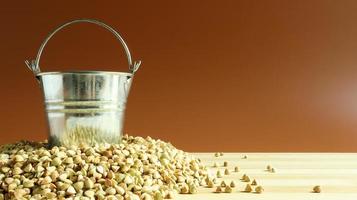 Small metal bucket with raw buckwheat on a board on a brown background. Organic vegetarian food. The concept of a healthy and balanced diet. Dietary nutrition. Copy space photo