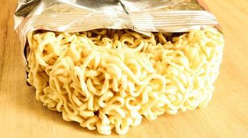 Raw dried instant noodles on a round wooden cutting board in an unnamed foil packaging with no name close up on a yellow background. pasta, for the preparation of which it is enough to pour water photo