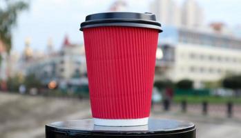 café en un vaso ecológico desechable de papel de color rojo con una tapa de plástico negro sobre el fondo de una calle de la ciudad. enfoque selectivo. primer plano del objeto. foto