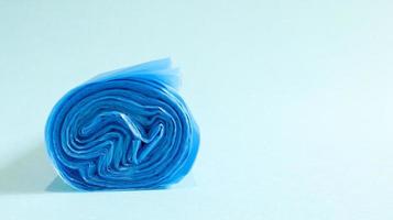 One roll of plastic trash bags in blue on a blue background. Bags that are designed to accommodate garbage in them and used at home and placed in various garbage containers. Copy space photo
