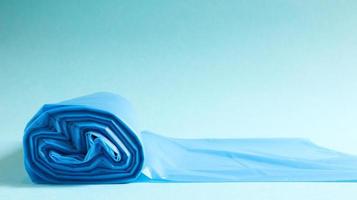 One roll of plastic trash bags in blue on a blue background. Bags that are designed to accommodate garbage in them and used at home and placed in various garbage containers. Copy space photo