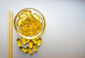 Fish oil capsules on a saucer with chopsticks. Bunch of vitamin omega 3 pills on a white background. Close-up, top view, high resolution product. Metabolism in the body. Body calcium. photo