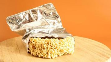 Raw dried instant noodles on a round wooden cutting board in an unnamed foil packaging with no name close up on a yellow background. pasta, for the preparation of which it is enough to pour water photo