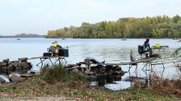 un pescador pesca en el río, vista trasera, desde el banco. un pescador se sienta en un puente de madera y piedra en la orilla del río e intenta pescar. deportes, recreación, estilo de vida foto