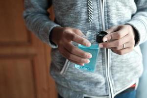 Sujete la mano un recipiente líquido de enjuague bucal contra el fondo azul. foto