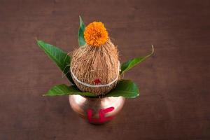 kalash de cobre con hojas de coco y mango con decoración floral sobre un fondo de madera. esencial en la puja hindú. foto