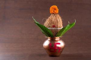 Copper kalash with coconut and mango leaf with floral decoration on a wooden background. essential in hindu puja. photo