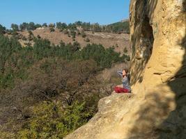 Woman with closed eyes and arms behind her head sitting on a mountain in the lotus position in meditation on an autumn day photo