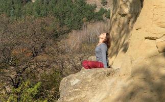 mujer con los ojos cerrados y con la cabeza en alto sentada en una montaña en posición de loto en meditación en un día de otoño foto