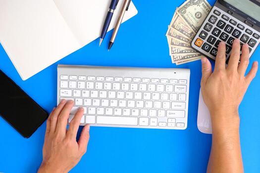 Blank notebook with pen are on top of blue office desk table with computer tools and supplies. Top view with copy space, flat lay. photo