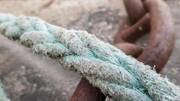 Blue colored aged boat manila rope placed on concrete road at the port. Dock with ropes and ropes. Metal mooring pole on concrete pier, selective focus photo