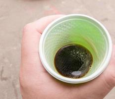 Green plastic cup with black coffee in a man's hand outdoors. A man holds a glass of coffee in his hand. View from above. photo