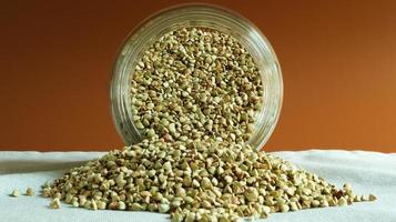 Scattered raw green buckwheat with a glass jar for cereals. Vegan organic food concept. The concept of diet, weight loss, healthy and proper nutrition. Triangle shaped scatter kernels photo