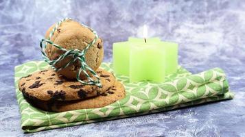 American chocolate chip cookies in a stack tied with thread on a green napkin and a candle. Traditional rounded crunchy dough with chocolate chips. Bakery. Delicious dessert, pastries. photo