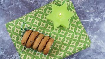 American chocolate chip cookies in a stack tied with thread on a green napkin and a candle. Traditional rounded crunchy dough with chocolate chips. Bakery. Delicious dessert, pastries. photo