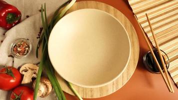 Round wooden board and plate, sauce and various vegetables on the table, wooden stick on a brown background. Flat lay. Copy space in the center of the frame for your text or logo. Recipe and Cooking photo