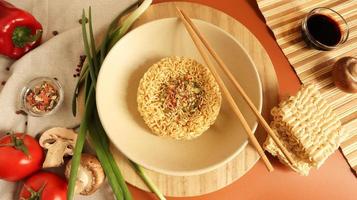 Instant noodles with king mushrooms, seasonings, soy sauce, peppers, green onions, tomatoes. Vegetable fast vegetarian soup. The process of cooking Asian food on the table. Vermicelli, spaghetti photo