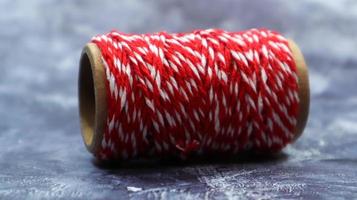 Baker's twine. Red and white lines. Red roll of woolen thread, close-up on gray marble background. Spool of decorative threads. photo