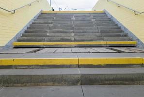 Empty yellow underground pedestrian crossing. Tunnel and daylight at the end. Steps to the top at the pedestrian crossing. A long concrete tunnel with lanterns in the city underground. photo