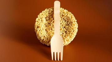 Raw instant noodles in the shape of a circle with a wooden disposable fork. pasta, for the preparation of which it is enough to pour boiling water and wait a few minutes. spaghetti. Copy space photo