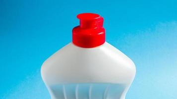 botella de plástico blanco con detergente para lavar platos, lejía o suavizante de telas sobre un fondo azul. detergente líquido en polvo. el concepto de limpieza. foto