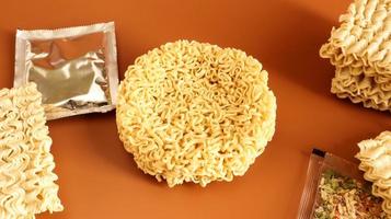 circle of instant noodles with raw spices on a plain brown background. Sprinkle dry Chinese or Korean vermicelli with salt and spices before pouring boiling water. pasta and flavors included photo