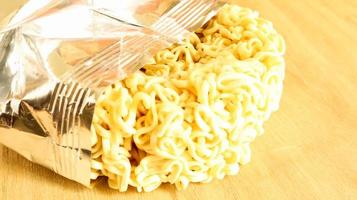 Raw dried instant noodles on a round wooden cutting board in an unnamed foil packaging with no name close up on a yellow background. pasta, for the preparation of which it is enough to pour water photo