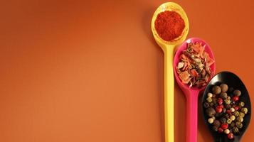Various spices in plastic spoons on a brown background. Copy space. A mixture of peppers, red smoked paprika, seasoning twelve vegetables. photo
