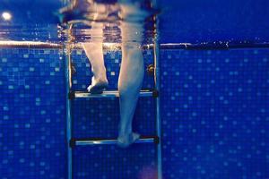 piernas de hombres en las escaleras bajo el agua en la piscina en verano foto