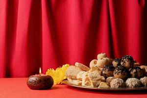 traditional indian sweets on red background with candles and flowers flat lay photo