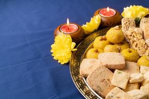 traditional indian sweets on blue background with candles and flowers flat lay photo