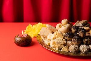 traditional indian sweets on red background with candles and flowers flat lay photo