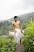 joven indio en forma, caminando por un camino al lado de los cultivos en el campo. un sacerdote indio caminando vestido con un dhoti blanco. hombre religioso indio. foto