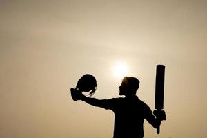 silueta de un jugador de cricket celebrando después de ganar un siglo en el partido de cricket. jugadores de críquet indios y concepto deportivo. foto