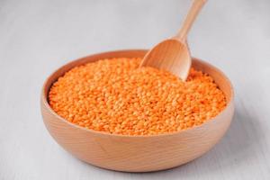 Raw red lentils in a wooden bowl and spoon on a white table photo