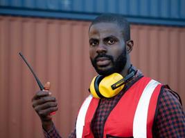 capataz ingeniero masculino supervisor sudáfrica piel negra brasileño sostener teléfono y mirar cámara sonrisa trabajo trabajo carrera logística importación exportación carga comercial comercio contenedor envío transporte foto