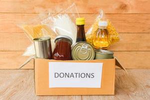 Donations box with canned food on wooden table background  pasta canned goods and dry food non perishable with cooking oil rice noodles spaghetti macaroni donations food photo