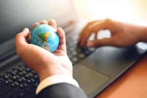 Business man holding earth globe model in hand and use a laptop - Business technology global and around the world concept photo