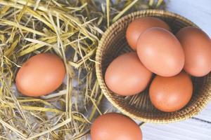 Fresh egg on basket and straw with wooden table background top view - Raw chicken eggs collect from the farm products natural eggs photo